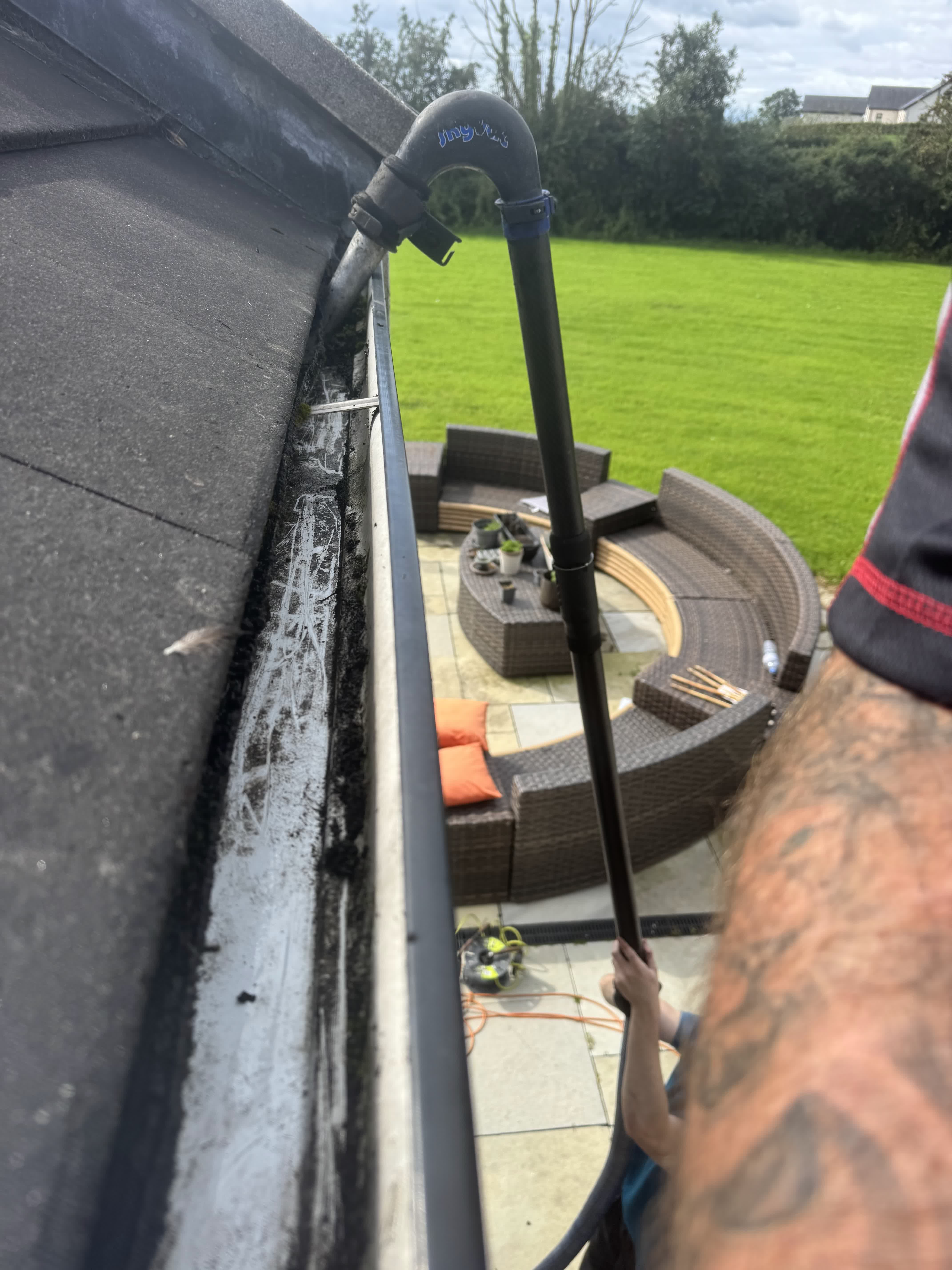 A gutter vacuum clearing a house gutter, seen from the roof, with the patio and garden below